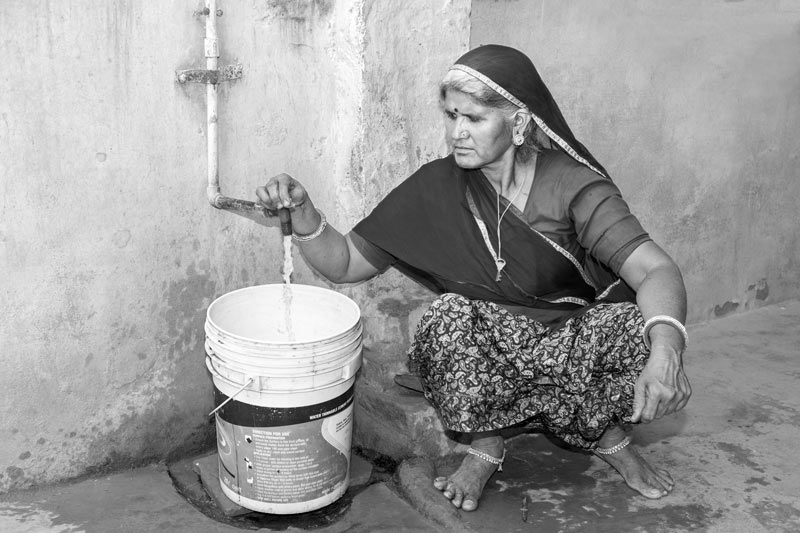 Industry and Violation of Human Right to Water - Logri Bai, 50 years, resident of Bichhadi, Udaipur district, Rajasthan, filling bucket with water sourced from the local tubewell-based pipeline supply